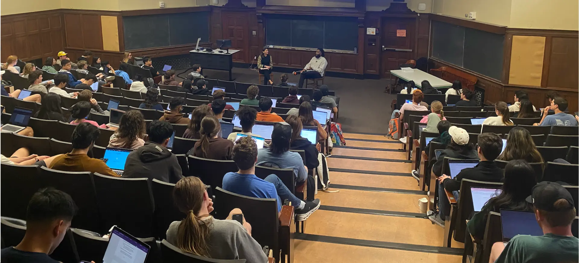 Jerold McDonald in conversation at the front of a full university lecture hall